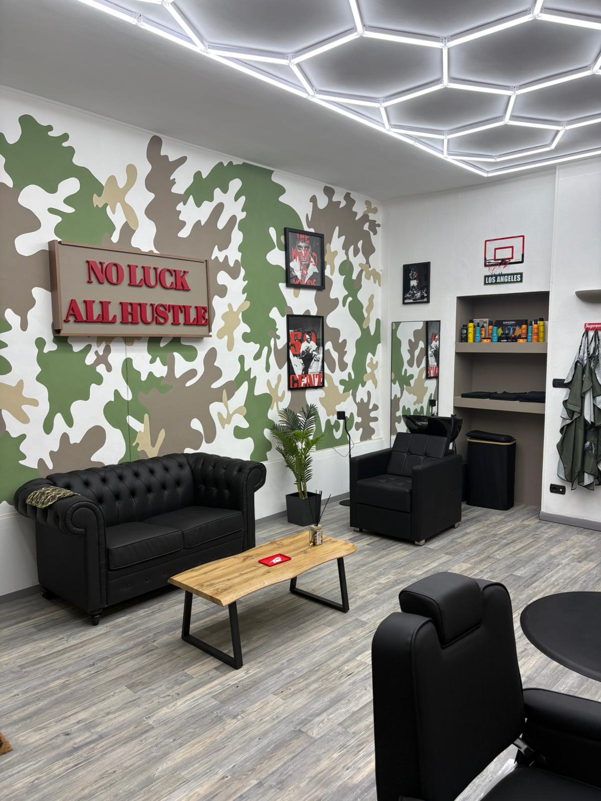Area attesa del Victory Lap Barber Shop con divano, tavolino e insegna sulla parete mimetica